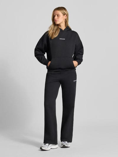Frauenmodel trägt Relaxed Fit Hoodie aus Baumwoll-Mix Modell 'Clarita' von PEGADOR in Schwarz mit Logo-Stickerei, Ganzkörperansicht von vorne.