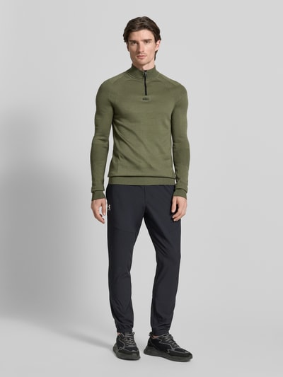 Männermodel trägt Regular Fit Troyer mit Schurwoll-Anteil Modell 'TOUR SEAMLESS QZ' von BOSS Green in Oliv, Jacquard, unifarben, Ganzkörperansicht von vorne.