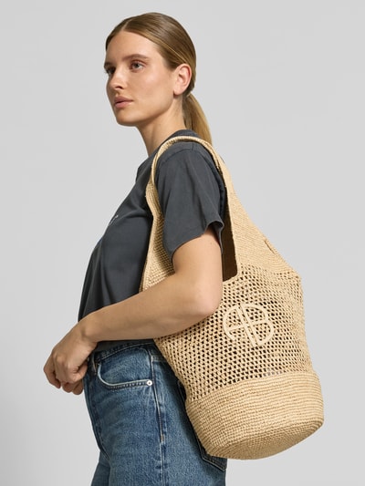 Vrouwenmodel draagt shopper met gaatjesmotief van Anine Bing, semi-transparante look, labelapplicatie, draagband, hoofdvak, zijaanzicht, KI-modified