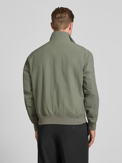 Männermodel trägt Relaxed Fit Blouson aus wasserafstotend materiaal model 'OPENS' van BOSS Orange, look: effen, lange mouw, opstaande kraag, tweewegritssluiting, labelpatch, geribd aan mouwboord en rompzoom, zij-steekzakken, Ganzkörperansicht Rückansicht.
