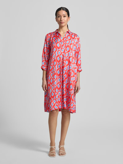Frauenmodel trägt knielanges Hemdblusenkleid mit V-Ausschnitt von Milano Italy in Rot mit geometrischem Allover-Muster, reine Viskose, A-Linie, Hemdblusenkragen, Ganzkörperansicht von vorne.