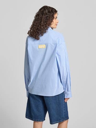 Frauenmodel trägt Relaxed Fit Bluse mit Label-Print von ANOTHER COTTON LAB in Hellblau mit weißen Streifen aus reiner Baumwolle, Ganzkörperansicht Rückansicht.