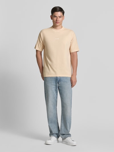 Männermodel trägt Relaxed Fit T-Shirt aus reiner Baumwolle Modell 'TE_TILE' von BOSS Orange in Optik: Unifarben mit Label-Stitching, Rundhals-Ausschnitt und Kurzarm; Ganzkörperansicht von vorne.