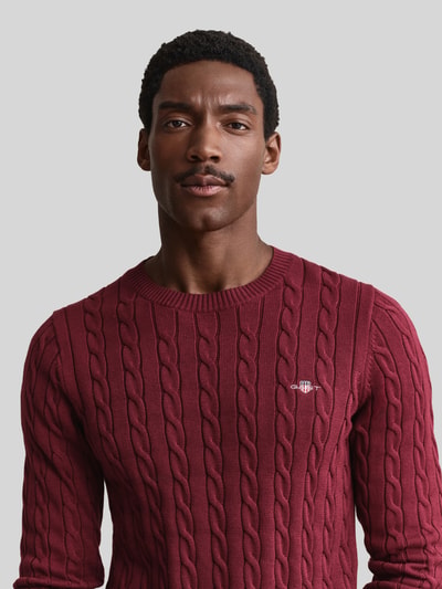 Männermodel trägt Regular Fit Pullover aus reiner Baumwolle von GANT in Dunkelrot mit Zopfmuster, Herren Pullover, Nahaufnahme Oberkörper.