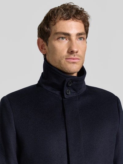 Männermodel trägt Mantel mit seitlichen Eingrifftaschen Modell 'Aleric' von Tiger of Sweden, dunkelblau, glatte Struktur, Nahaufnahme Oberkörper.