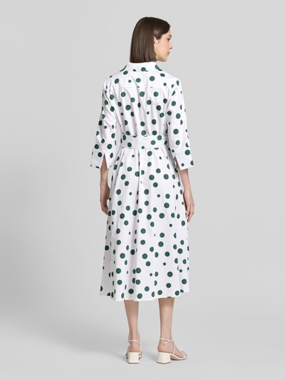 Frauenmodel trägt Hemdblusenkleid aus reiner Baumwolle von Christian Berg Woman, weiß mit grünen Punkten, Taillienband, 3/4-Arm, Rückenansicht Ganzkörperansicht. Passform tailliert, Hemdblusenkragen, durchgängige Knopfleiste, Rückenlänge bei Größe 36: 121 cm, Brustweite 46 cm, Ärmellänge 48 cm.