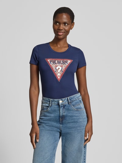 Vrouwenmodel draagt T-shirt met logo en ronde hals van guess in donkerblauw, mix van katoen en elastaan, slim fit, ruglengte maat S 58 cm, nahaufnahme bovenlichaam.