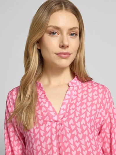 Vrouwenmodel draagt blouse uit zuiver viscose met serafinohals model 'Ja44nina' van ZABAIONE, los model, roze met witte harten, close-up bovenlichaam.