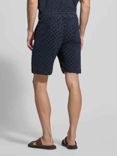 Männermodel trägt Regular Fit Shorts mit Label-Patch von Lindbergh aus Baumwoll-Mix in Dunkelblau mit Eingrifftaschen und Gesäßtasche, Ganzkörperansicht Rückansicht.