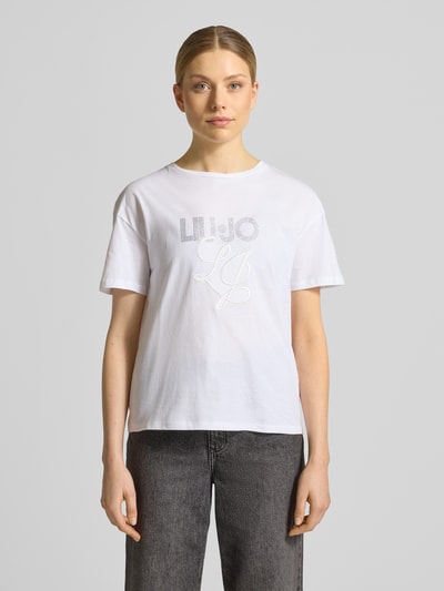 Frauenmodel trägt T-Shirt mit Label-Stitching und Ziersteinbesatz von Liu Jo White in Weiß, Reine Baumwolle, Regular-Fit, Rundhalsausschnitt, Rückenlänge bei Größe S 56 cm, Ganzkörperansicht von vorne.