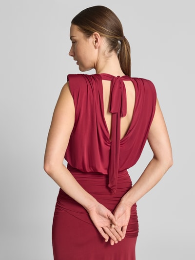 Frauenmodel trägt Abendkleid mit Drapierungen und Wasserfall-Ausschnitt von Lipsy in Rot, figurbetont, Material-Mix, Rückseitige Schnürung, Detailaufnahme Rückenansicht.