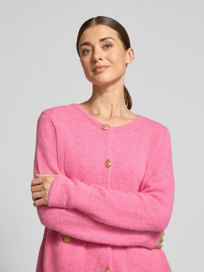 Vrouwenmodel draagt Strickjacke mit Rundhalsausschnitt und Knopfleiste van Milano Italy in felroze, zachte textuur, regular fit, opgestikte zakken met knoopsluiting, nahaufnahme bovenlichaam.