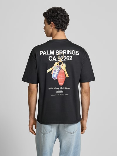 Männermodel trägt Boxy Fit T-Shirt aus reiner Baumwolle Modell 'FRED ESCAPE' von Only & Sons, schwarz, Motiv-Print, Ganzkörperansicht Rückansicht