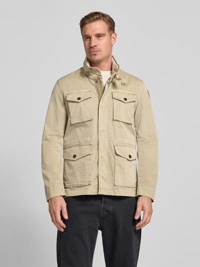 Męski model nosi kurtkę Jacke mit Stehkragen und Pattentaschen Modell 'Ashmont' von Blauer Usa, mieszanka bawełny i elastanu, krój regular fit, jasny beż, stójka, kieszenie z patką, długość tyłu w rozmiarze M: 72 cm, szerokość ramion w rozmiarze M: 40 cm, szerokość klatki piersiowej w rozmiarze M: 52 cm, długość rękawów w rozmiarze M: 63 cm, przód, zdjęcie całej sylwetki.