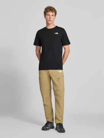 Mannenmodel draagt t-shirt met labelprint Model 'Evolution' van The North Face in zwart, katoenmix, regular fit, ruglengte bij maat M 73 cm, geheelopname voorkant.