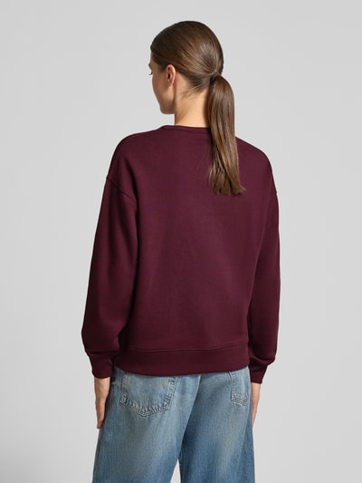 Frauenmodel trägt Relaxed Fit Sweatshirt aus reiner Baumwolle von GANT in Dunkelrot mit glatter Textur zu blauen Jeans, Ganzkörperansicht Rückansicht.