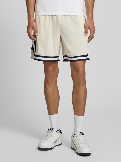 Männermodel trägt Regular Fit Shorts mit elastischem Bund von KARL KANI in Beige mit Strukturmuster und Logo-Stitching, Nahaufnahme Unterkörper. Bundweite 38 cm, Innenbeinlänge 21 cm, Herren Shorts.