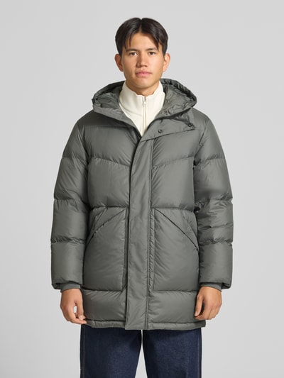 Männermodel trägt Regular Fit Steppmantel mit Kapuze von Marc O'Polo DENIM in Olivgrün mit glatter Oberfläche, Ganzkörperansicht von vorne.