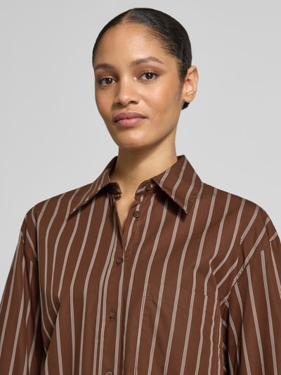 Frauenmodel trägt Relaxed Fit Hemdbluse mit Brusttasche Modell 'LLAMA' von Mango aus reiner Baumwolle mit Streifenmuster, Nahaufnahme Oberkörper.