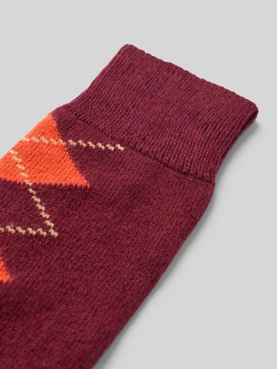 Produktfoto, Socken mit Kaschmir-Anteil im Karo-Design von UNIO HAMBURG, bawełniany miks z dodatkiem kaszmiru, ściągacze prążkowane, wzór w kratę, widoczna tekstura dzianiny, odcienie bordowego i pomarańczowego