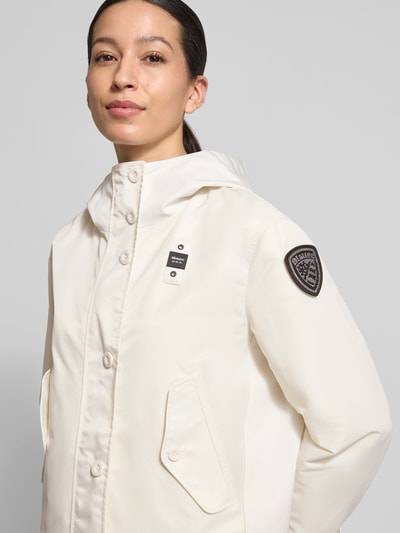 Frauenmodel trägt Jacke mit Label-Patches Modell 'MARCELA' von Blauer Usa in Creme mit Kapuze und Knopfverschluss, Nahaufnahme Oberkörper.