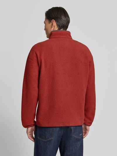 Männermodel trägt Fleecepullover mit Label-Patch Modell 'Helvetia™ II' von Columbia in Rot, grobe Textur, Ganzkörperansicht Rückansicht. Gerader Schnitt, Stehkragen, kurze Knopfleiste, Brusttasche mit Reißverschluss, Rückenlänge 70 cm, Ärmellänge 62 cm.