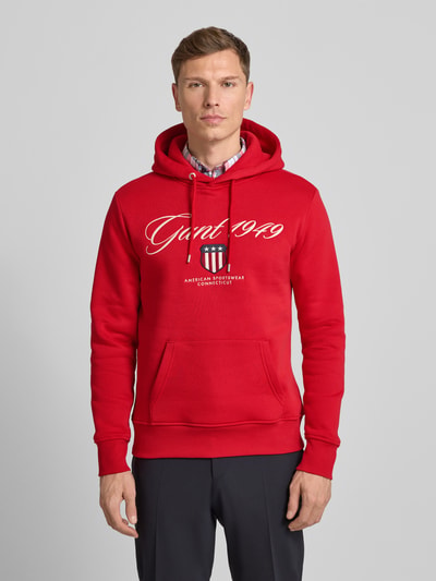 Męski model nosi Hoodie mit Label-Stitching und Känguru-Tasche od Gant w kolorze czerwonym, bawełniany, Regular Fit, przód, ujęcie całopostaciowe.