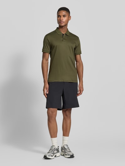 Männermodel trägt Regular Fit Poloshirt aus reiner Baumwolle Modell 'PS Spirit 70 Plk' von BOSS Green X PORSCHE, Oliv, Ganzkörperansicht von vorne.