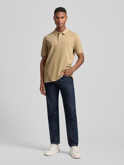 Männermodel trägt Regular Fit Poloshirt aus reiner Baumwolle Modell 'DONOS222' von HUGO in Beige mit Label-Applikation, Ganzkörperansicht von vorne.