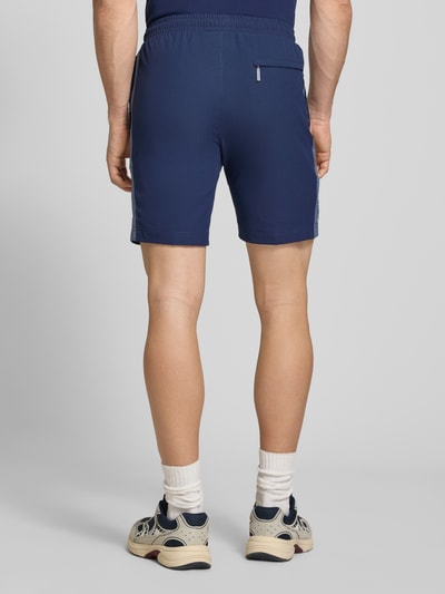 Männermodel trägt Shorts mit Logo-Print Modell 'GOCCIA' von SERGIO TACCHINI in Dunkelblau, lockerer Schnitt, Rückansicht Ganzkörperansicht.