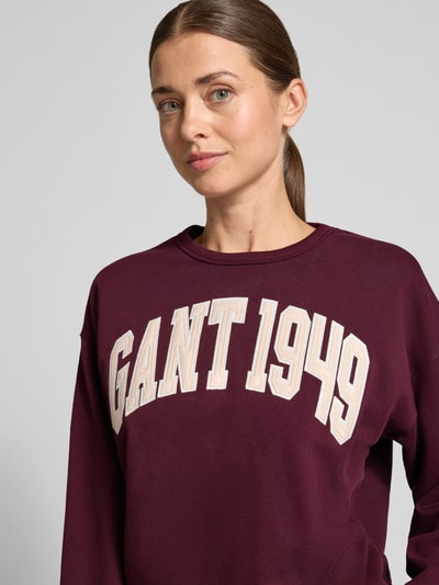 Frauenmodel trägt Relaxed Fit Sweatshirt aus reiner Baumwolle von GANT in Dunkelrot mit cremefarbenem Logo, glatte Textur, Nahaufnahme Oberkörper. Damen Sweatshirt von GANT.