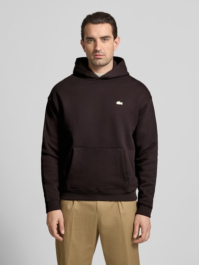 Männermodel trägt Regular Fit Hoodie aus reiner Baumwolle von Lacoste in Optik: Unifarben mit Label-Patch, Kängurutaschen, Sweat, Ganzkörperansicht von vorne.