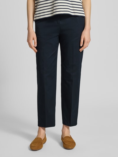 Frauenmodel trägt Tapered Chino aus Baumwoll-Mix Modell 'TECARINO2' von BOSS, Optik: Unifarben, Passform: Tapered, Mid Waist, Logo-Applikation, Bügelfalten, Gürtelschlaufen, Verschluss: Schiebehaken und verdeckter Reißverschluss, Eingrifftaschen, Gesäßtaschen, dunkler Farbton, glatte Textur, Ganzkörperansicht von vorne.
