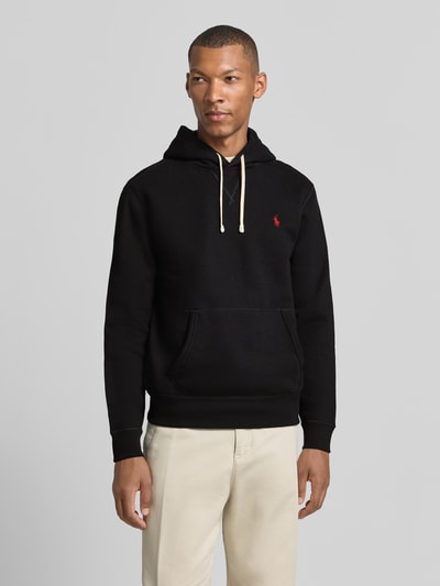 Mannelijk model draagt zwarte regular fit hoodie uit katoenmix met rood logo en beige broek van Polo Ralph Lauren, vooraanzicht bovenlichaam