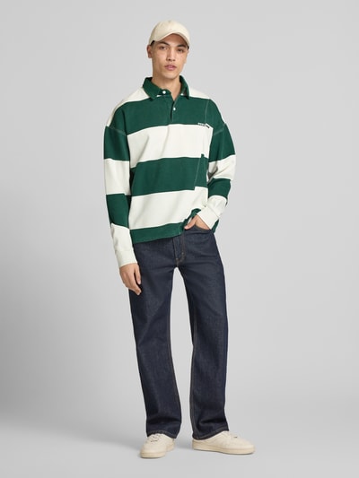 Męskimodel nosi koszulkę polo Relaxed Fit Poloshirt aus reiner Baumwolle Modell 'Castelluccio' von Pegador, ciemnozielone i białe szerokie pasy, wyhaftowane logo, krój relaxed fit, kołnierzyk polo z listwą guzikową, ściągacze na rękawach, długość tyłu w rozmiarze M: 69 cm, bawełna, Ganzkörperansicht von vorne.