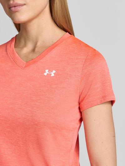 Vrouwenmodel draagt T-Shirt met V-hals en logo van Under Armour in regular fit, koraalroze kleur, logo op borst, detailopname bovenlichaam. Ruglengte maat S: 61 cm.