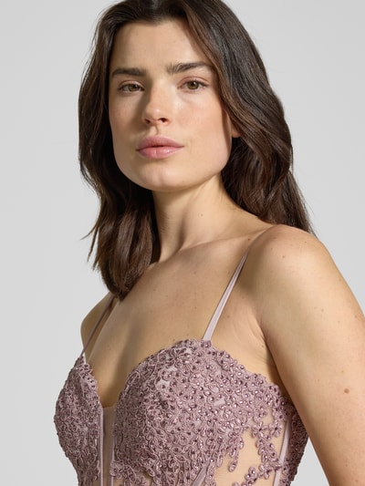 Frauenmodel trägt Abendkleid mit floralem Spitzenbesatz von Mascara in Mauve mit Ziersteinen und Spaghettiträgern, Nahaufnahme Oberkörper. Kontext: Taillierte Passform, Herz-Ausschnitt, semitransparentes Design, Nahtreißverschluss, rückseitige Schnürung, Maxilänge, Rockteil aus Satin, Rückenlänge bei Größe 36: 154 cm, Brustweite bei Größe 36: 41 cm.
