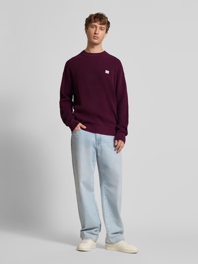 Męski model nosi Strickpullover mit Strukturmuster und Rundhalsausschnitt od Calvin Klein Jeans z bawełny, krój relaxed fit, widok całej sylwetki z przodu.