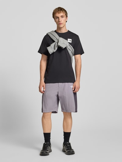 Mężczyzna nosi Shorts mit Logo und Gürtel von The North Face, szaro-czarne, krój regular fit, pasek, logo, elastyczny pas, szerokość w rozmiarze M: 42 cm, długość nogawki wewnętrznej: 24 cm, całopostaciowy widok z przodu.