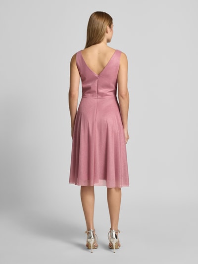 Frauenmodel trägt knielanges Cocktailkleid mit V-Ausschnitt von TROYDEN COLLECTION, rosafarbener Chiffon, Taillierter Schnitt, Rückseitiger V-Ausschnitt, Rückenlänge 85 cm, Brustweite 43 cm, Ganzkörperansicht Rückansicht.