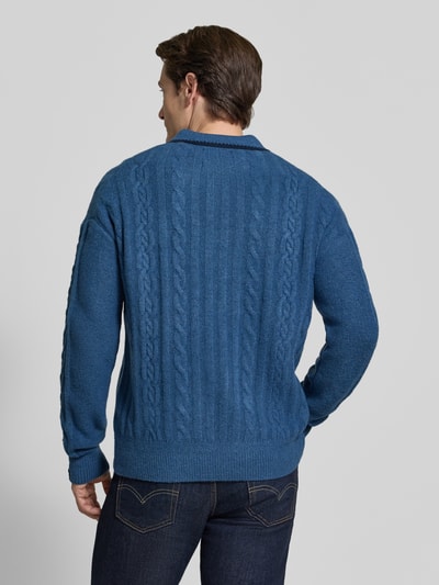 Männermodel trägt Regular Fit Strickpullover mit Woll-Anteil von Scotch & Soda in Blau, Zopfmuster, elastische Abschlüsse, Ganzkörperansicht Rückansicht.