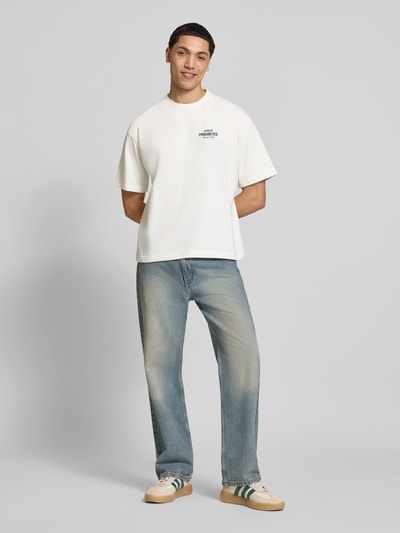 Männermodel trägt Regular Fit T-Shirt aus reiner Baumwolle Modell 'IN A RUSH' von PROHIBITED, helles Weiß mit Label-Stitching, Ganzkörperansicht von vorne. Rückenlänge bei Größe M: 67 cm.