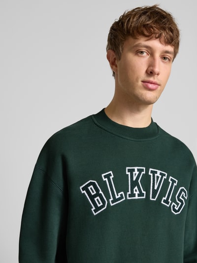 Männermodel trägt Sweatshirt mit Logo und Rundhalsausschnitt von BLKVIS, Relaxed-Fit, reine Baumwolle, dunkelgrün, Nahaufnahme Oberkörper.