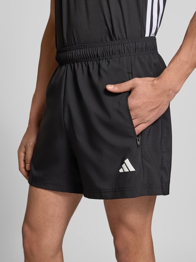 Männermodel trägt Regular Fit Sport-Shorts mit Logo-Print von adidas Training, Optik: Unifarben, seitliche Reißverschlusstasche, Nahaufnahme Oberschenkel.