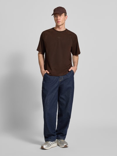 Männermodel trägt T-Shirt mit Rundhalsausschnitt und Label-Stitching von adidas Originals aus reiner Baumwolle, Relaxed-Fit, Ganzkörperansicht von vorne.