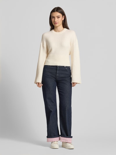 Frauenmodel trägt Strickpullover mit weiten Ärmeln Modell 'Stella' von Gina Tricot, Material-Mix mit Alpaka-Anteil, Regular-Fit, Rundhalsausschnitt, Rückenlänge 55 cm, Ärmellänge 60 cm, Cremefarben, glatte Struktur, vorne Ganzkörperansicht.