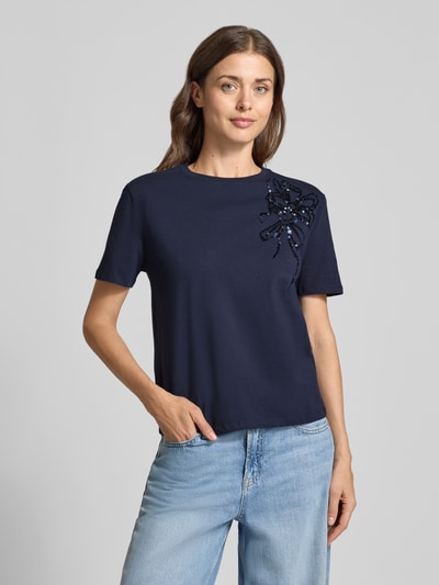 Frauenmodel trägt Regular Fit T-Shirt aus reiner Baumwolle mit Blumen-Applikation von Christian Berg Woman in Dunkelblau, Nahaufnahme Oberkörper. Rückenlänge bei Größe S: 54 cm, Pailletten, Rundhalsausschnitt, kurze Ärmel, überschnittene Schultern.