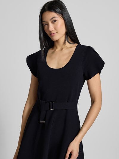 Kobiece modelka nosi sukienkę mini z mieszanki wiskozy model 'Ronella' od Ted Baker, taliowany krój, pasek w talii, okrągły dekolt, z krótkim rękawem, czarny kolor, tekstura gładka, Szerokość w rozmiarze 36: 42 cm, Długość tyłu: 84 cm, Długość rękawów: 16 cm, ujęcie z przodu, zbliżenie na górną część ciała.