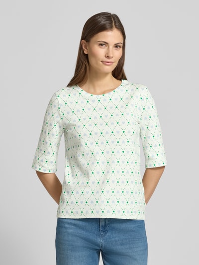 Frauenmodel trägt Regular Fit Longsleeve mit Allover-Motiv-Print von Marc Cain in Weiß mit grün-blauem Muster, Halbarm, Vorderansicht, Nahaufnahme Oberkörper. Elastischer Baumwoll-Mix, Rundhalsausschnitt, Rückenlänge 57 cm bei Größe 36.