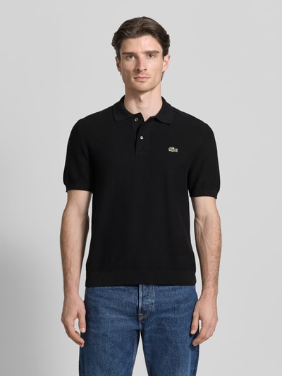Męski model nosi Regular Fit Poloshirt aus reiner Baumwolle od Lacoste, czarna bawełna, krój regular fit, logo, krótki rękaw, widok na całe ciało z przodu.